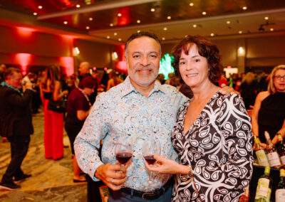 Man and woman hold wine glasses smiling at camera at wine event.
