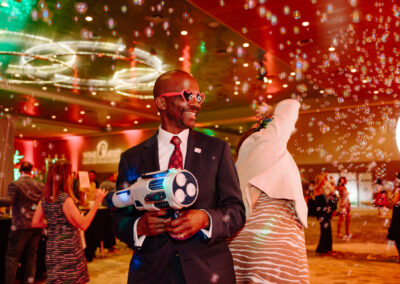 Man in suit is posing for a 360 selfie camera at wine quest shooting bubbles from a bubble maker.