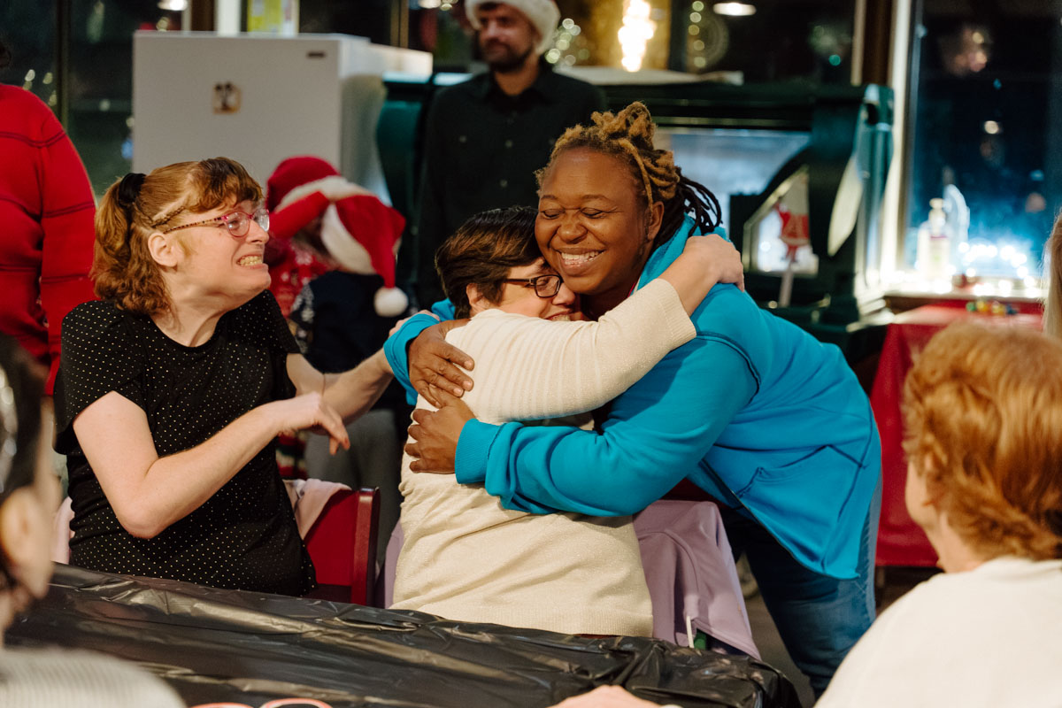 Client and volunteer embraced in a hug at the holiday home adoption party at Quest's Camp Thunderbird.